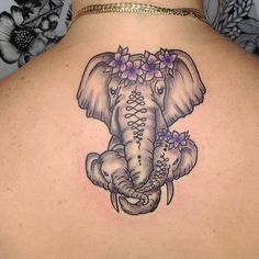 an elephant tattoo on the back of a woman's upper body, with flowers around its trunk