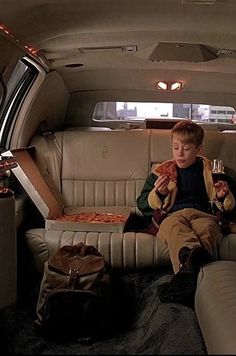 a young boy sitting in the back seat of a car eating pizza and drinking wine