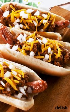 three chili cheese hot dogs are on a cutting board