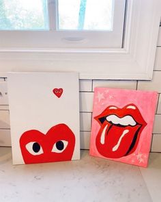 two paintings are sitting on the counter in front of a window, one is red and the other is white