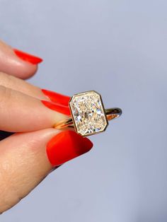 a woman's hand holding a ring with a diamond in it and red nail polish