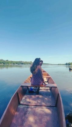 a woman sitting in the bow of a boat on a lake with trees around her