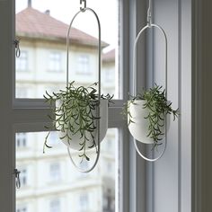 two hanging planters with plants in them on a window sill next to a building