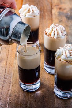 someone is pouring something into three glasses filled with coffee and whipped cream on a wooden table