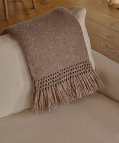 a white couch with a brown blanket on it's back and wooden floors in the background