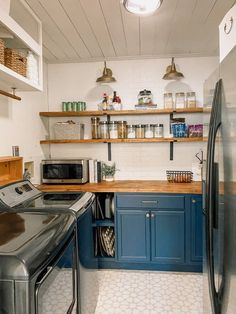 a kitchen with blue cabinets and white tile flooring, an open shelving above the washer and dryer