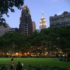 people sitting on benches in the middle of a park at night with skyscrapers in the background