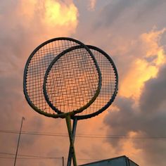 a giant tennis racket sitting on top of a metal pole in front of a cloudy sky