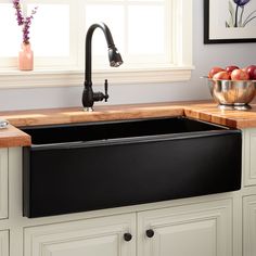 a black kitchen sink sitting under a window next to a counter top with fruit on it