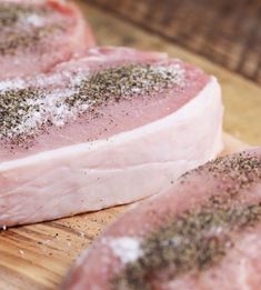 raw pork chops on a cutting board with seasoning sprinkled on them