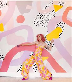 a woman with pink hair is posing in front of a colorful wall