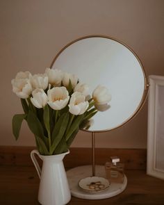 white tulips in front of a round mirror on a table with a gold stand