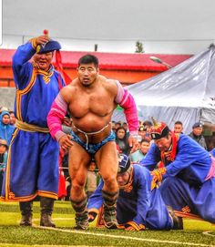 two sumo wrestlers in blue and pink wrestling outfits, with spectators watching them from the sidelines