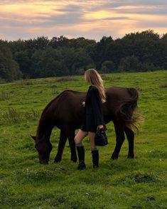 a woman standing next to a brown horse on top of a lush green field