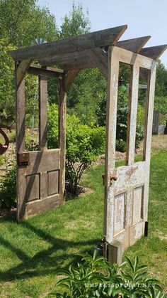 an old wooden door is open in the grass next to a garden area with trees and bushes