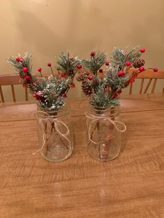 two mason jars filled with pine cones and red berries are sitting on a wooden table