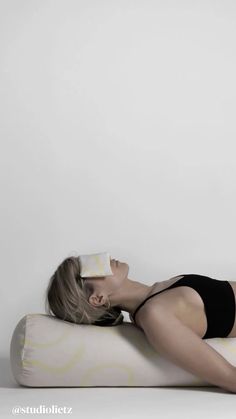 a woman laying on top of a pillow while wearing a black bathing suit and holding an object in her mouth