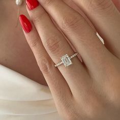 a woman's hand with red nail polish holding a diamond ring and pearl necklace