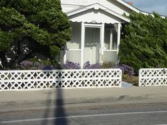 a small white house sitting on the side of a road next to trees and bushes