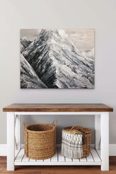 a painting hanging on the wall above a white table with two baskets and a basket underneath it