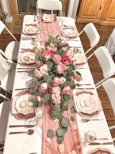 the table is set with pink and white plates, silverware, and floral centerpieces