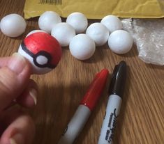 a hand holding a red and white ball next to two pens on top of a wooden table