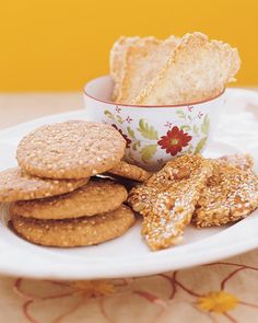 a white plate topped with cookies and crackers next to a cup filled with powdered sugar