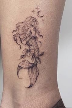 a woman's thigh with a tattoo design on the side of her leg and an image of a mermaid sitting on top of it