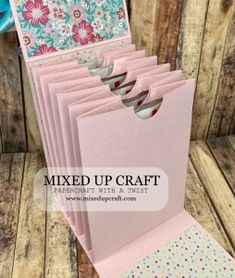 a stack of pink cards sitting on top of a wooden table next to a blue vase