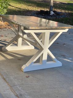 a wooden table sitting on top of a cement floor next to a tree and grass