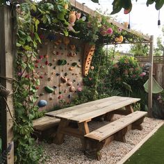 a wooden picnic table sitting in front of a wall with plants and rocks on it