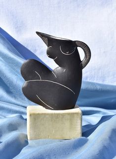 a black sculpture sitting on top of a white block in front of a blue sheet