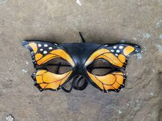 a yellow and black butterfly mask sitting on top of a cement floor next to a wall