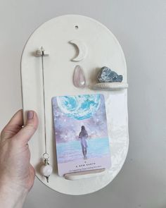 a person holding up a book next to a moon and crystal necklace on a wall