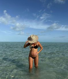 a woman standing in the ocean wearing a hat