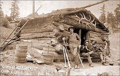 an old black and white photo of men in front of a log cabin