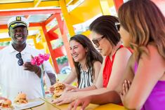 a group of people sitting at a table eating sandwiches and smiling for the camera man