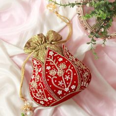 a red and gold purse sitting on top of a pink blanket next to a plant