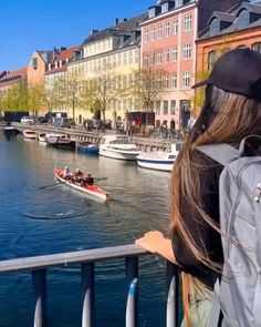 a woman looking out over the water at boats on the river and buildings in the background