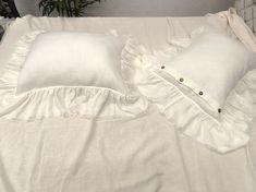 two white pillows sitting on top of a bed next to a plant in a vase