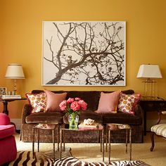 a living room filled with furniture and flowers on top of a coffee table in front of a painting