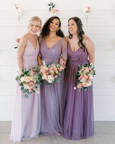 three bridesmaids in long purple dresses smiling at the camera with their bouquets