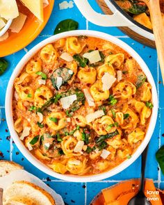 a bowl of pasta with spinach, cheese and bread on a blue tablecloth