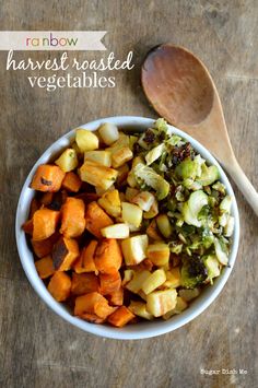 a white bowl filled with roasted vegetables next to a wooden spoon on top of a table