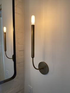 a wall mounted light next to a mirror in a room with white walls and flooring