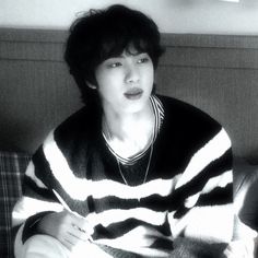 a young man sitting on top of a couch wearing a striped shirt and black and white sweater