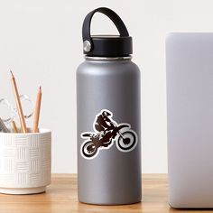 a person riding a dirt bike on the back of a silver water bottle next to a white laptop