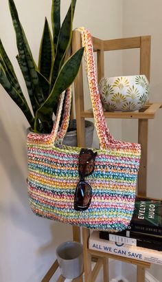 a multicolored bag sitting on top of a wooden stand next to a potted plant