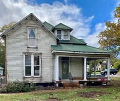 an old house with a green roof and white trim on the front porch is shown