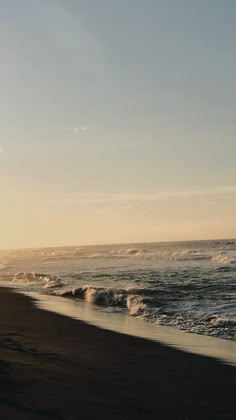 a person walking on the beach with a surfboard in their hand and waves crashing against the shore